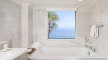 A bathroom with a large bathtub, a window with a view of the sea, and a marble wall.