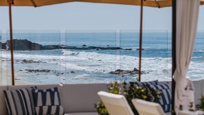 A beach view from a balcony with umbrellas, a sofa, and a chair. - Surf & Sand Laguna Beach (Laguna Beach)