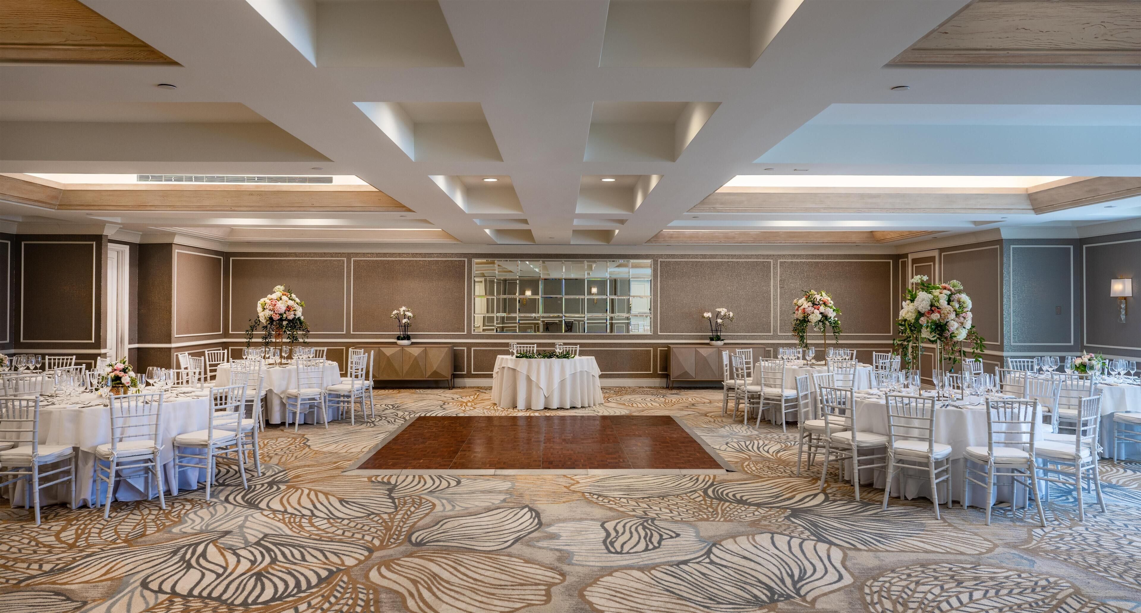 Une salle de banquet avec des tables rondes, des chaises blanches et des centres de table floraux.