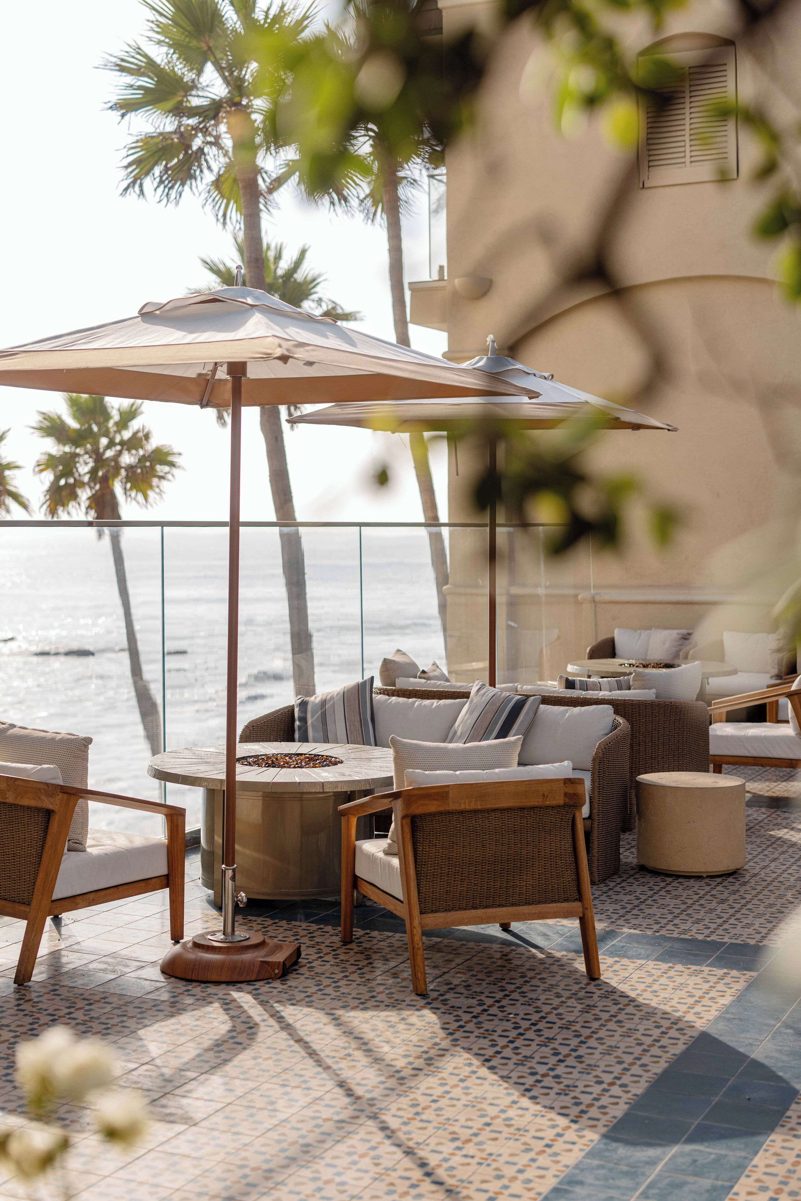 Eine Terrasse am Meer mit Korbmöbeln, einem großen Sonnenschirm und Blick auf den Ozean.