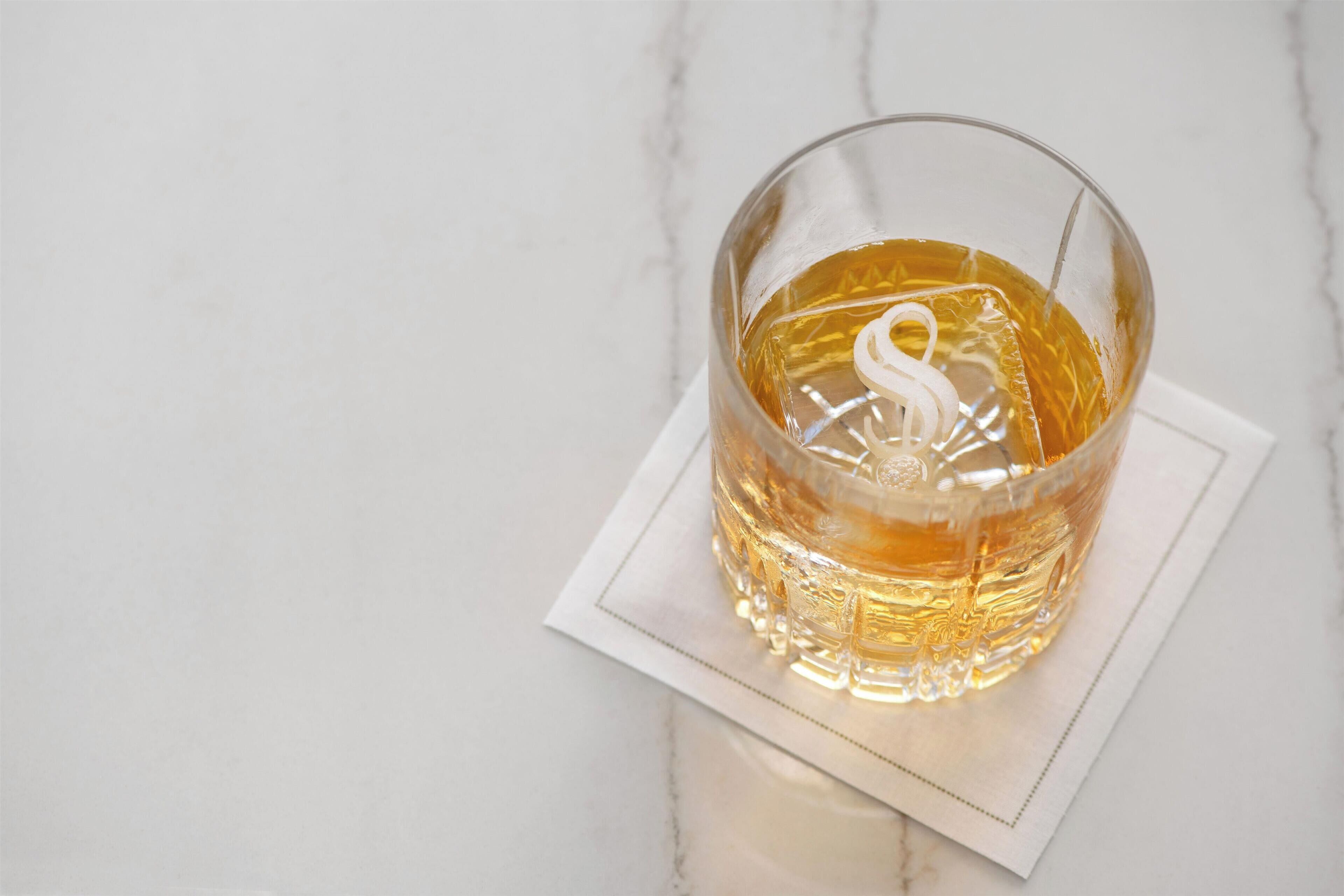 A clear glass with a golden liquid on a white napkin on a marble surface.