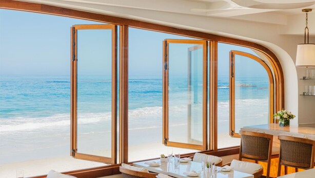 A beachfront restaurant with tables and chairs, large windows with wooden frames, and a view of the ocean. - Surf & Sand Laguna Beach (Laguna Beach)