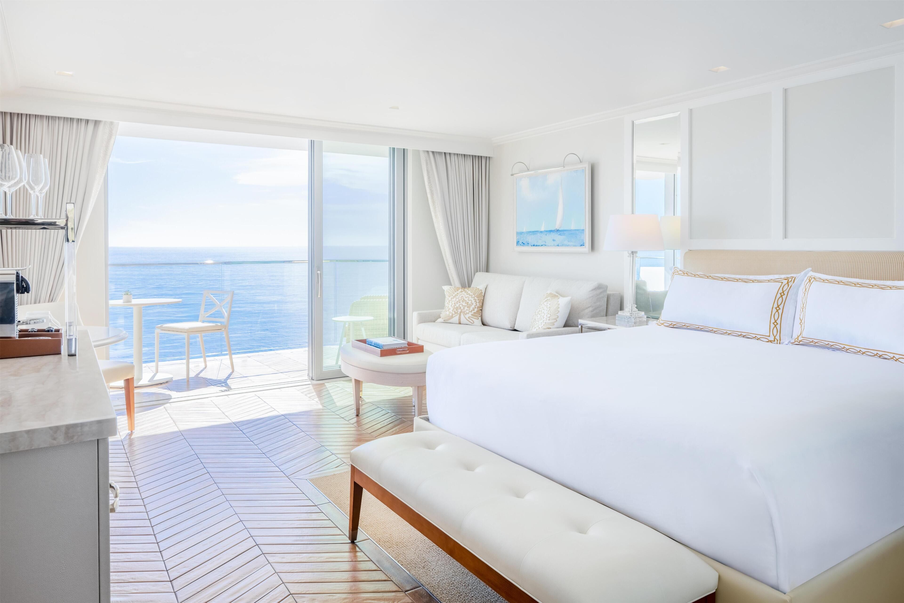 A bedroom with a large bed, a sofa, a small table, and a view of the sea.