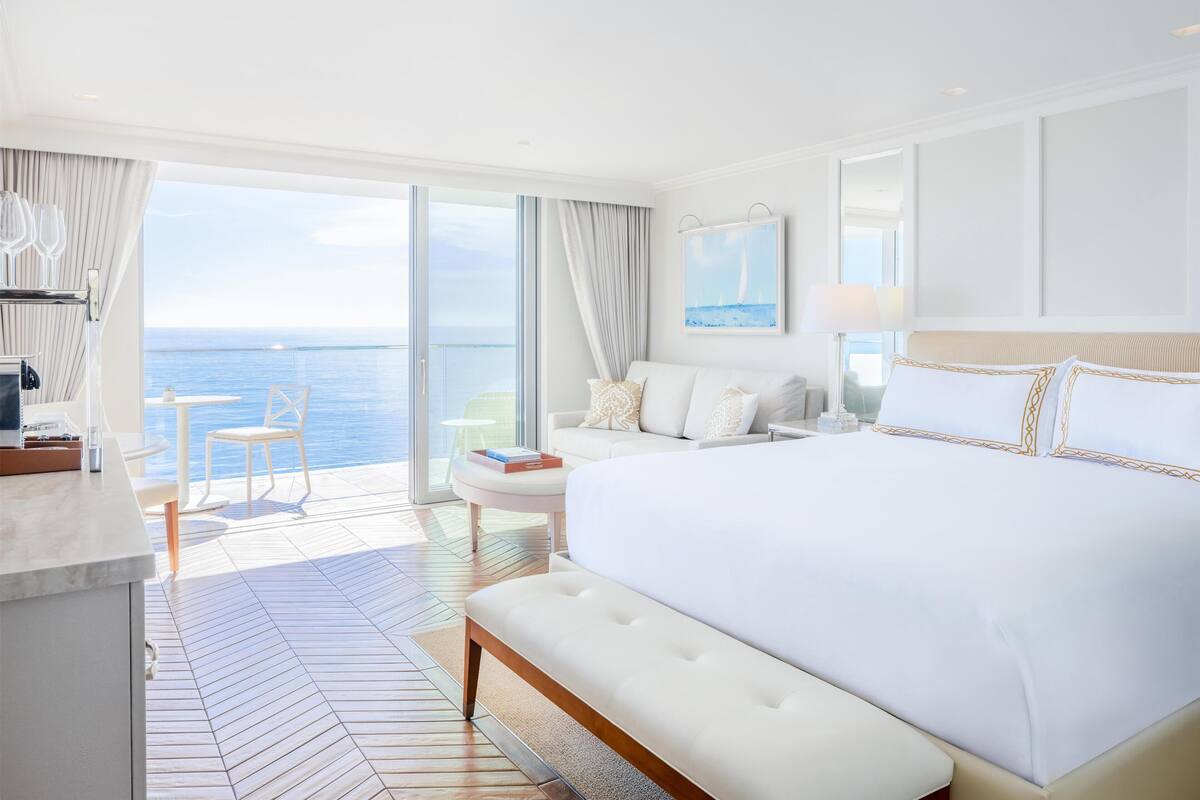 A bedroom with a large bed, a sofa, a small table, and a view of the sea.