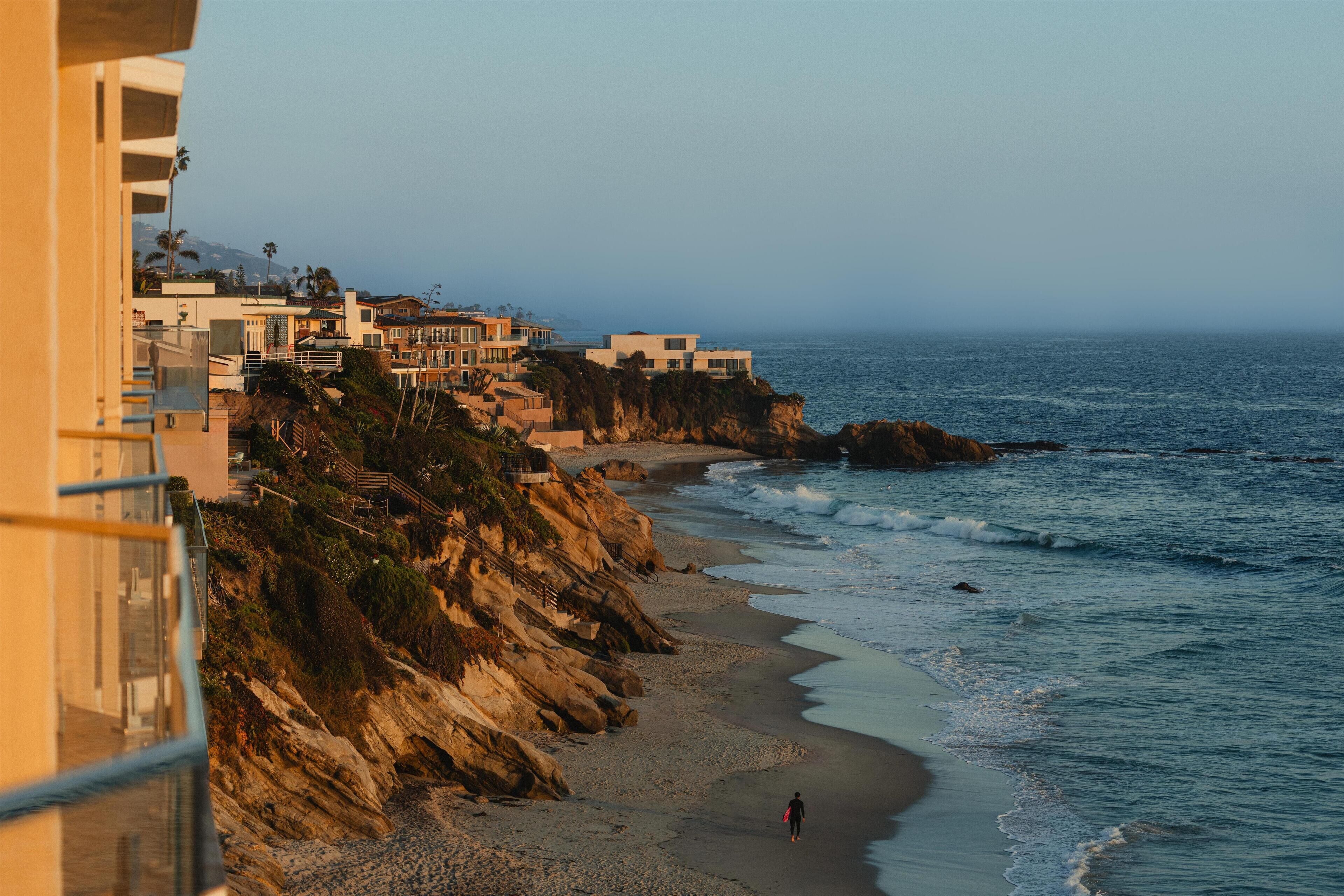 A coastal hotel with a beach view, a rocky cliff, and a person walking on the beach.