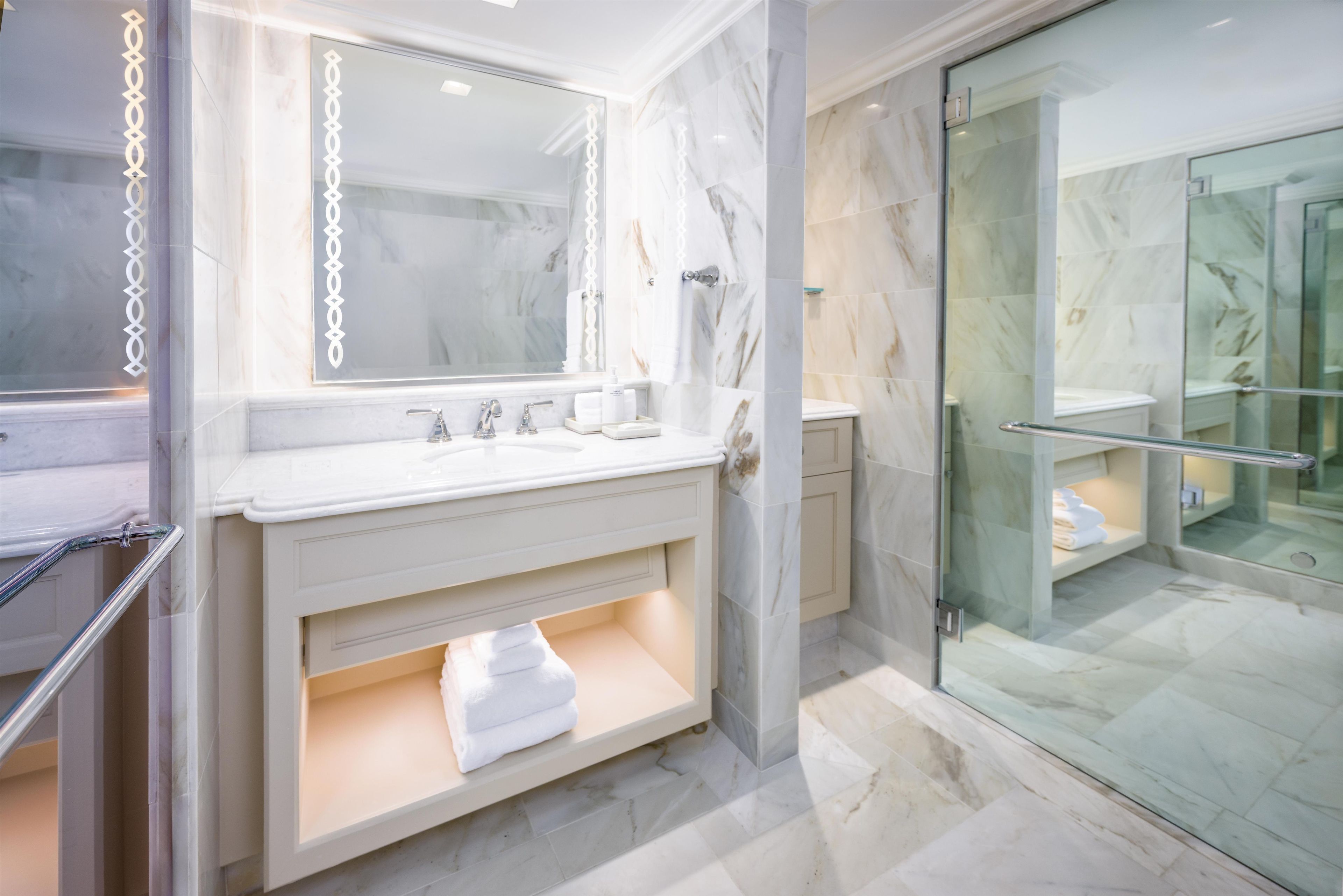 Un bagno moderno con cabina doccia in vetro, un mobile lavabo con specchio e pavimento in marmo.