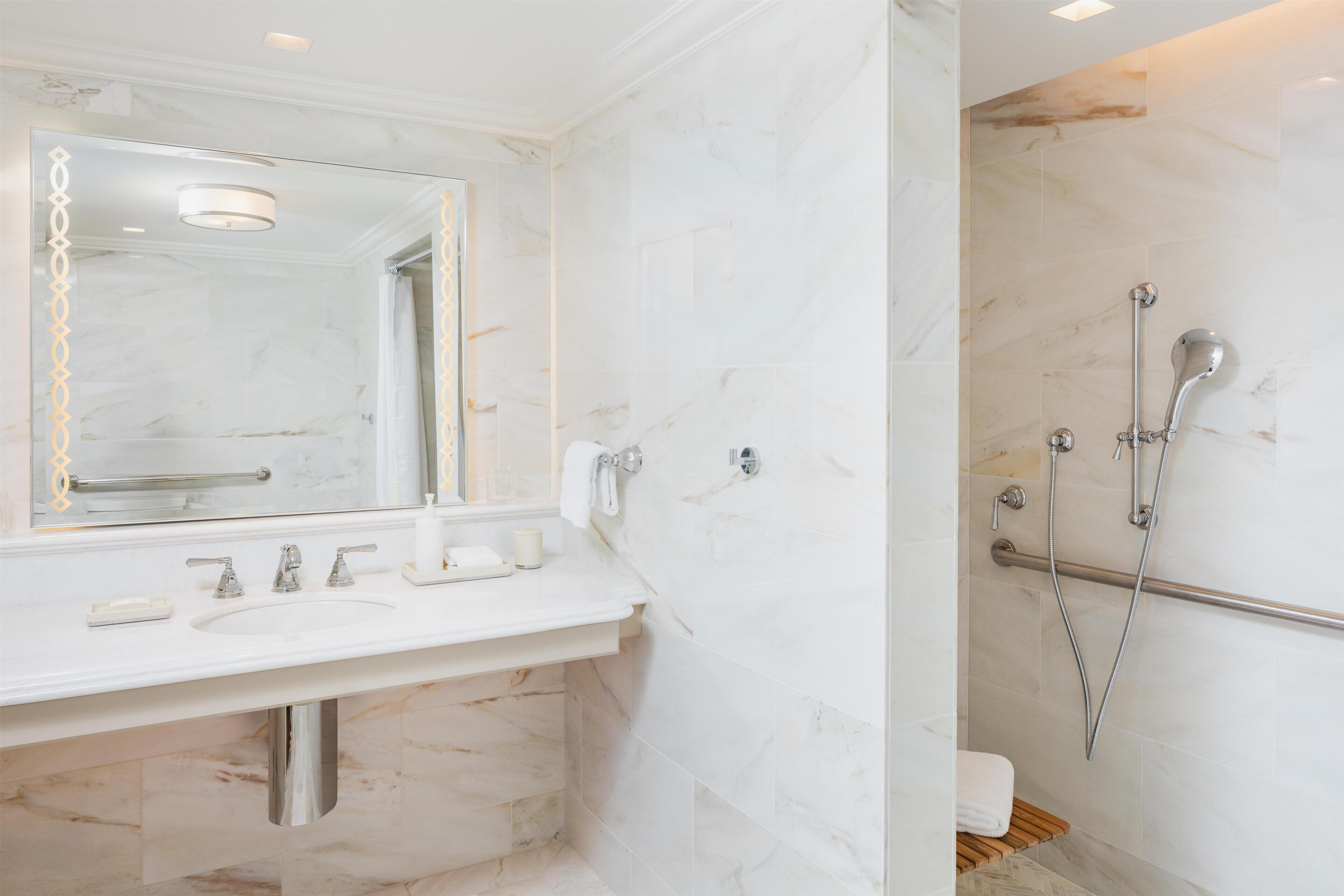 A bathroom with a marble sink, a large mirror, a shower with a handheld showerhead, and a towel rack.