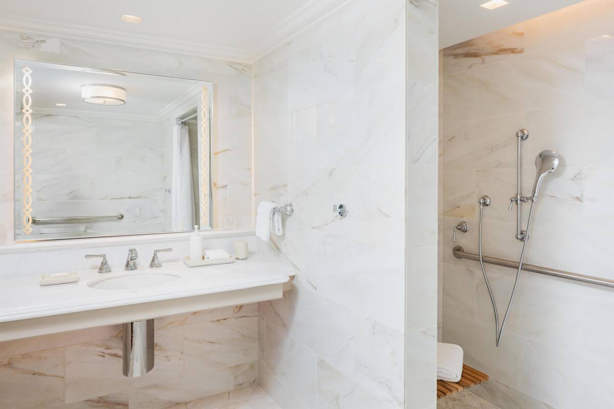 A bathroom with a marble sink, a large mirror, a shower with a handheld showerhead, and a towel rack.