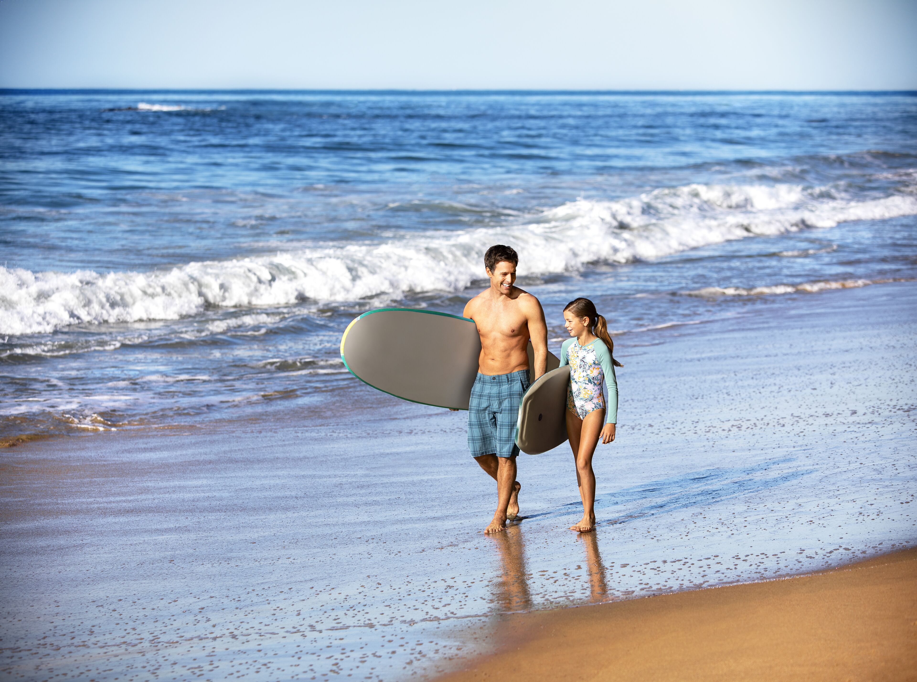 A beach scene with two people walking, one holding a surfboard.