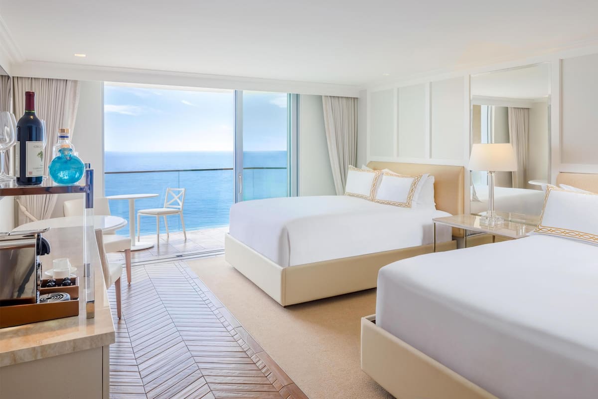 A hotel room with two beds, a dining area, and a view of the sea.
