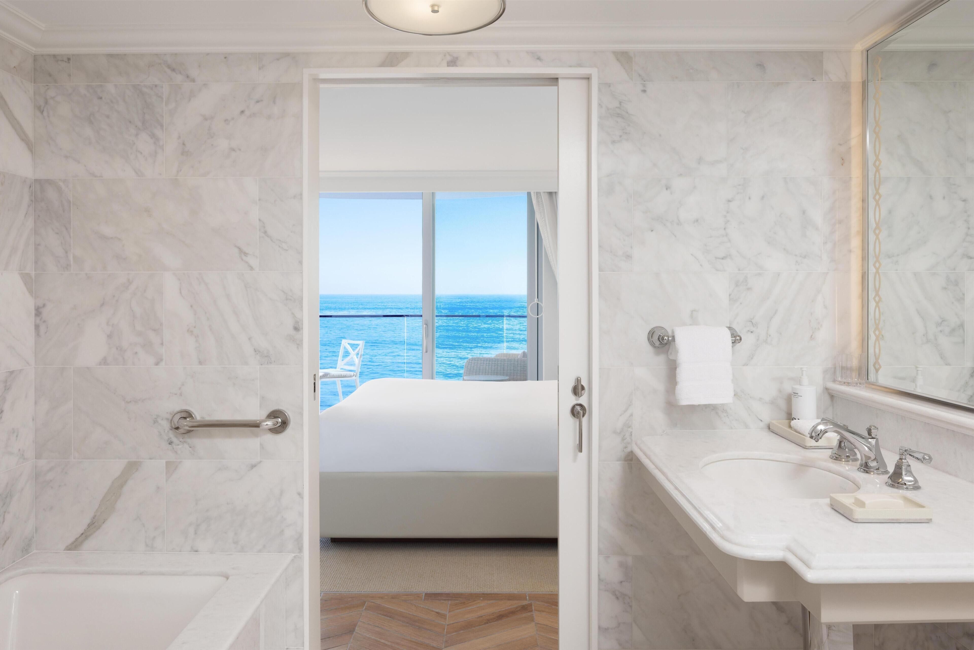 Ett hotellrum med ett badrum i marmor, en stor säng och utsikt över havet.
