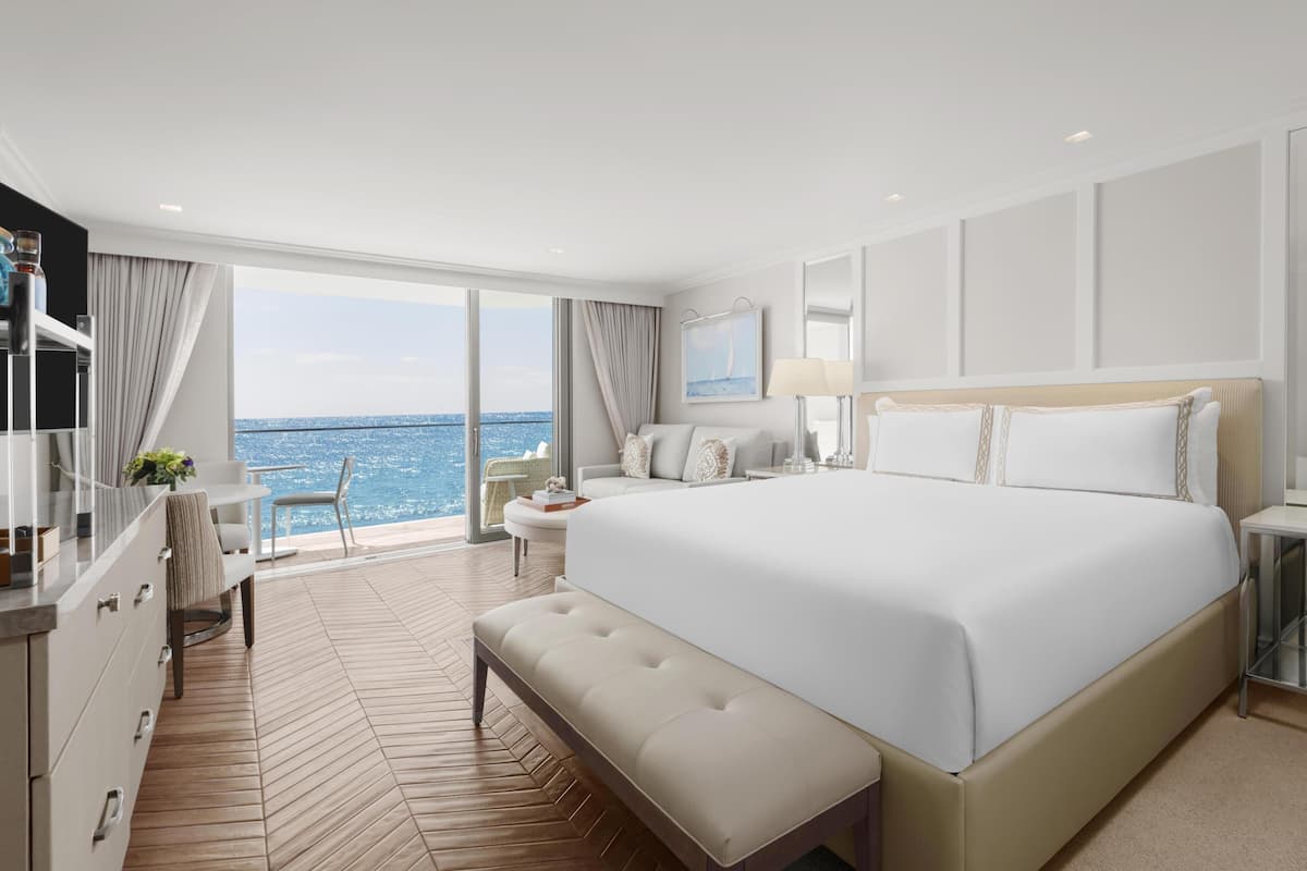 A modern hotel room with a large bed, a desk, and a view of the ocean.