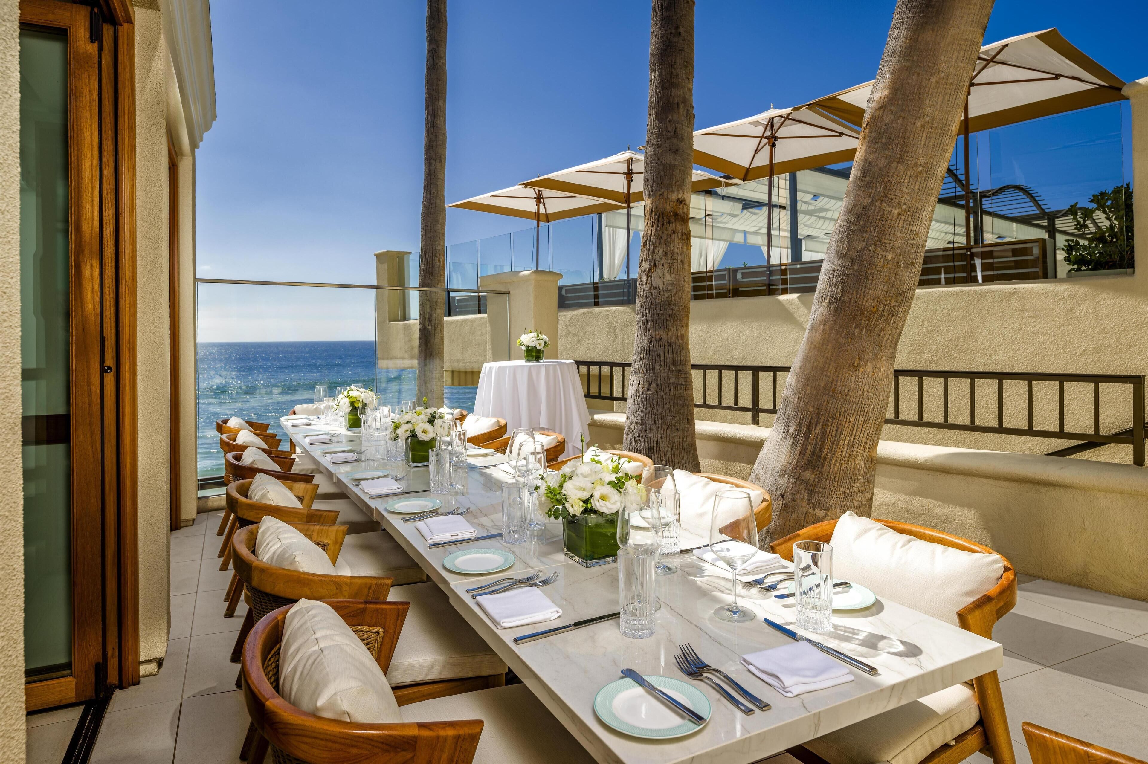 A long dining table set for a meal with white tablecloths, floral centerpieces, and wooden chairs.
