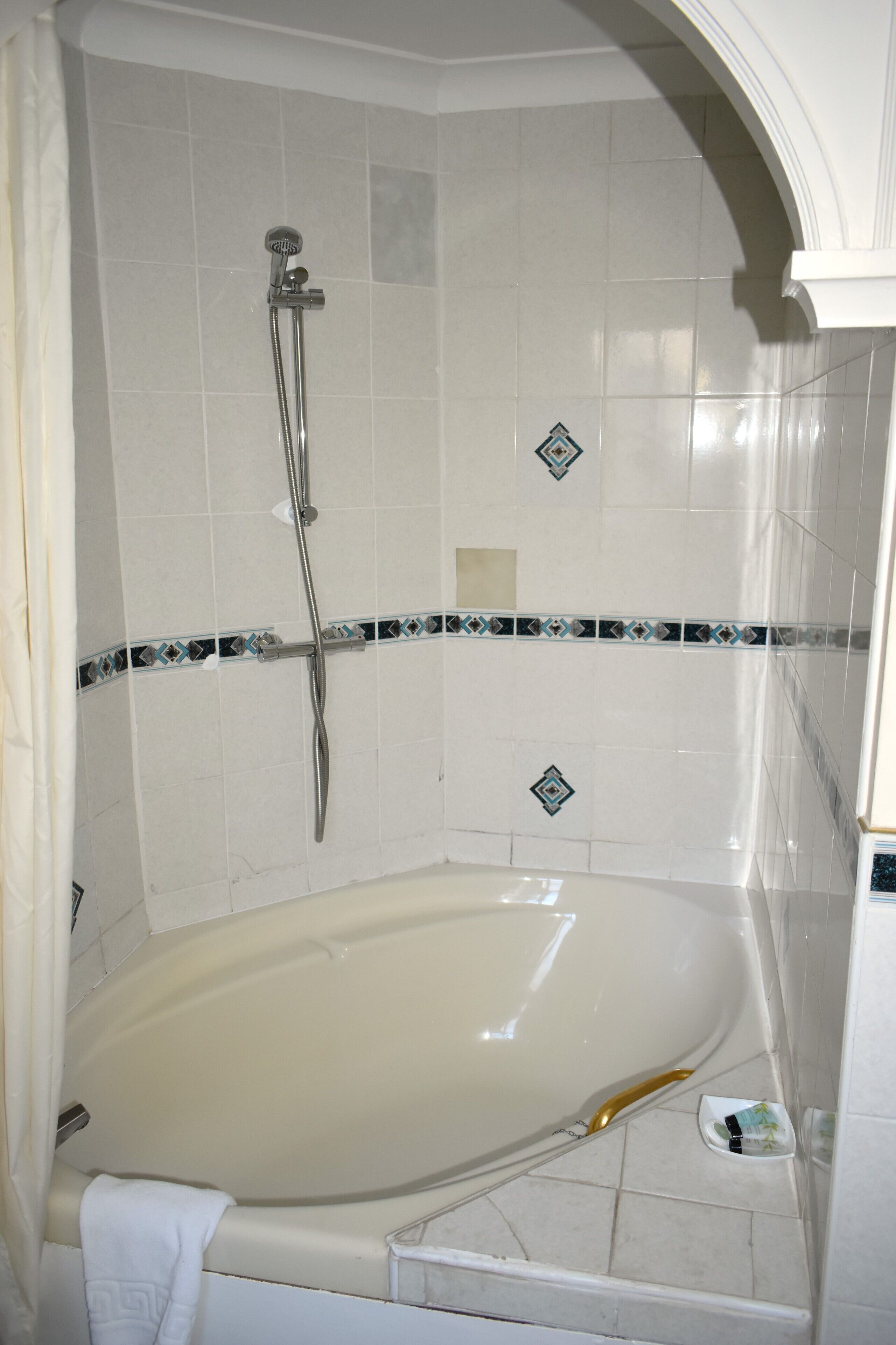Un baño con bañera, cabezal de ducha y azulejos decorativos.