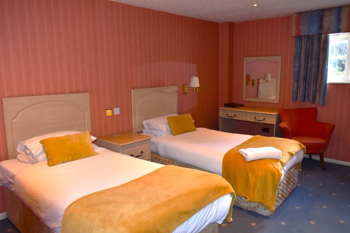 A hotel room with two beds, a desk, a chair, and a mirror.