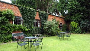 A brick building with ivy-covered walls and a grassy lawn. There are metal tables and chairs arranged on the lawn. - Donington Manor Hotel (Derby)