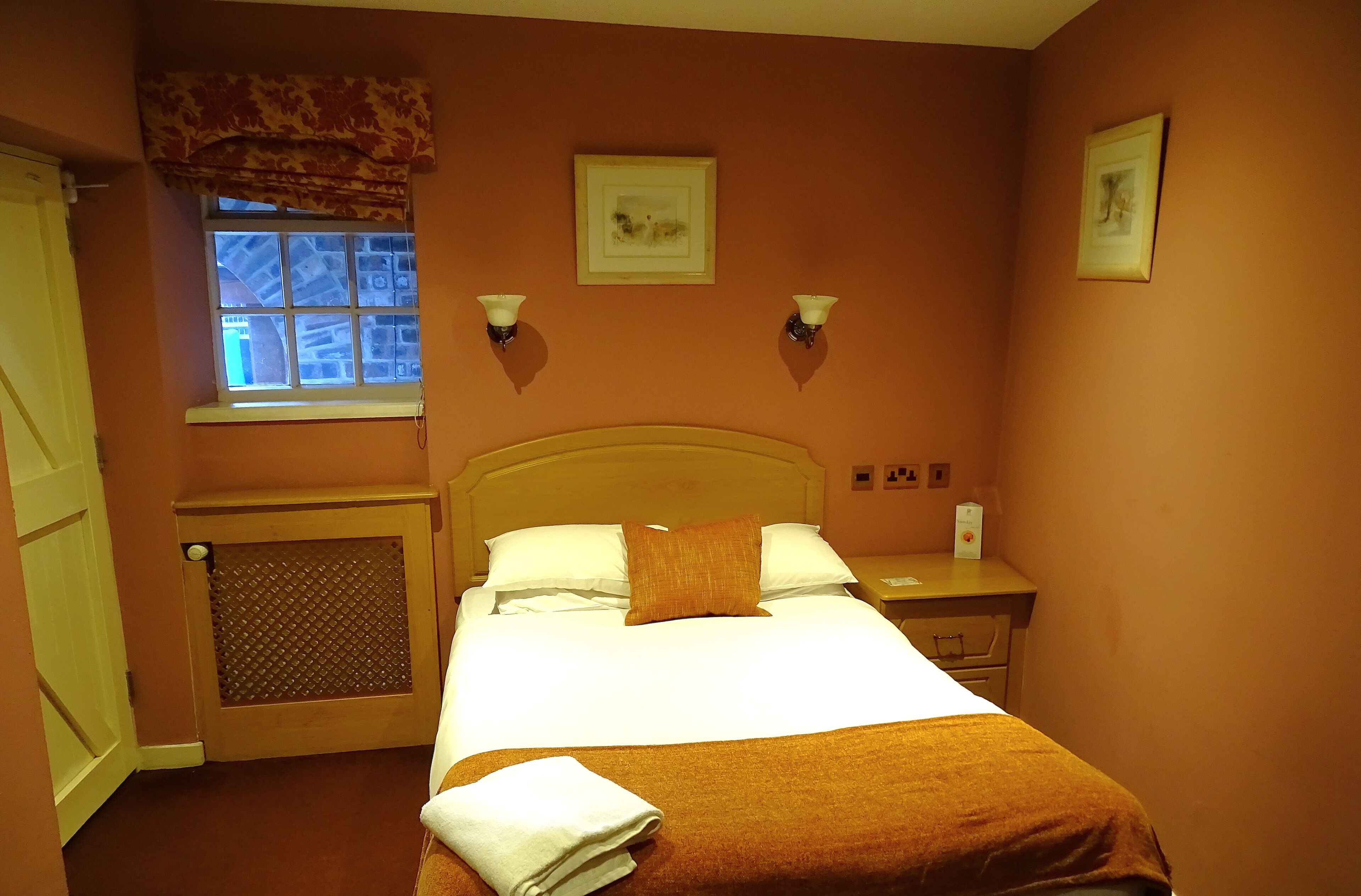 Quarto de hotel com cama, janela com vista, mesa de cabeceira e quadro na parede.