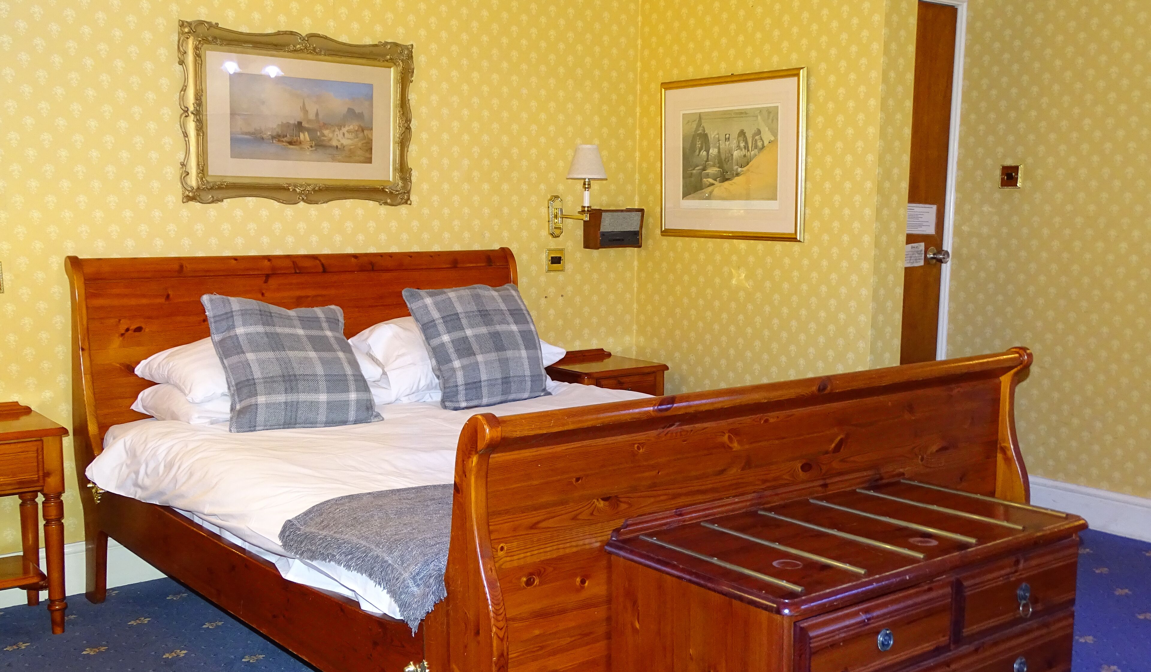 Ein hölzernes Bett mit Kopfteil, zwei Nachttische, ein Beistelltisch und eine Holzkommode.