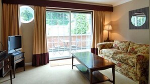 A living room with a sofa, a television on a stand, a table, and a large window with curtains. - Donington Manor Hotel (Derby)
