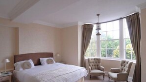 A bedroom with a large bed, two chairs, a nightstand, and a window with curtains. - Donington Manor Hotel (Derby)