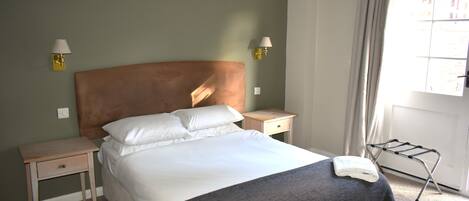 A neatly made bed with a headboard, two bedside tables, a lamp, and a window with curtains.