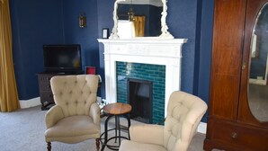 Una habitación con dos sillones, una pequeña mesa de madera, un televisor, una chimenea y un mueble de madera grande.
