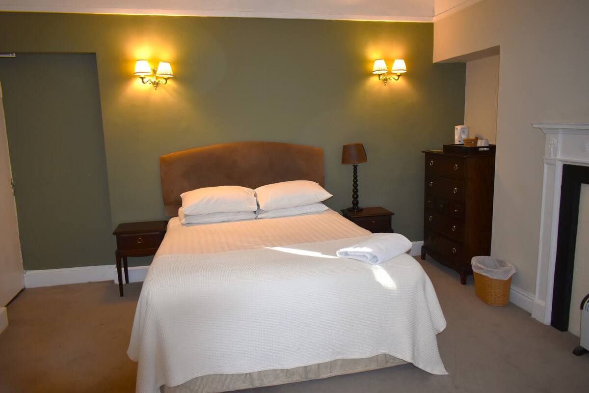 A neatly made bed with white linens, a wooden headboard, and two wall-mounted lamps.