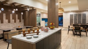 A modern kitchen with a central island, wooden chairs, and a fruit display. - Mobile Marriott (Mobile)