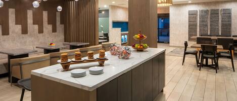 A modern kitchen with a central island, wooden chairs, and a fruit display.