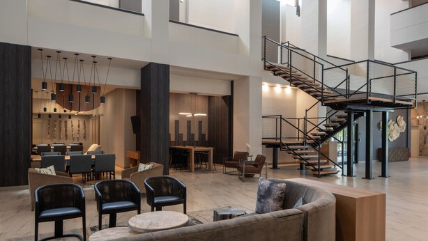 A spacious lobby with a modern staircase, seating areas, and a dining space. - Mobile Marriott (Mobile)