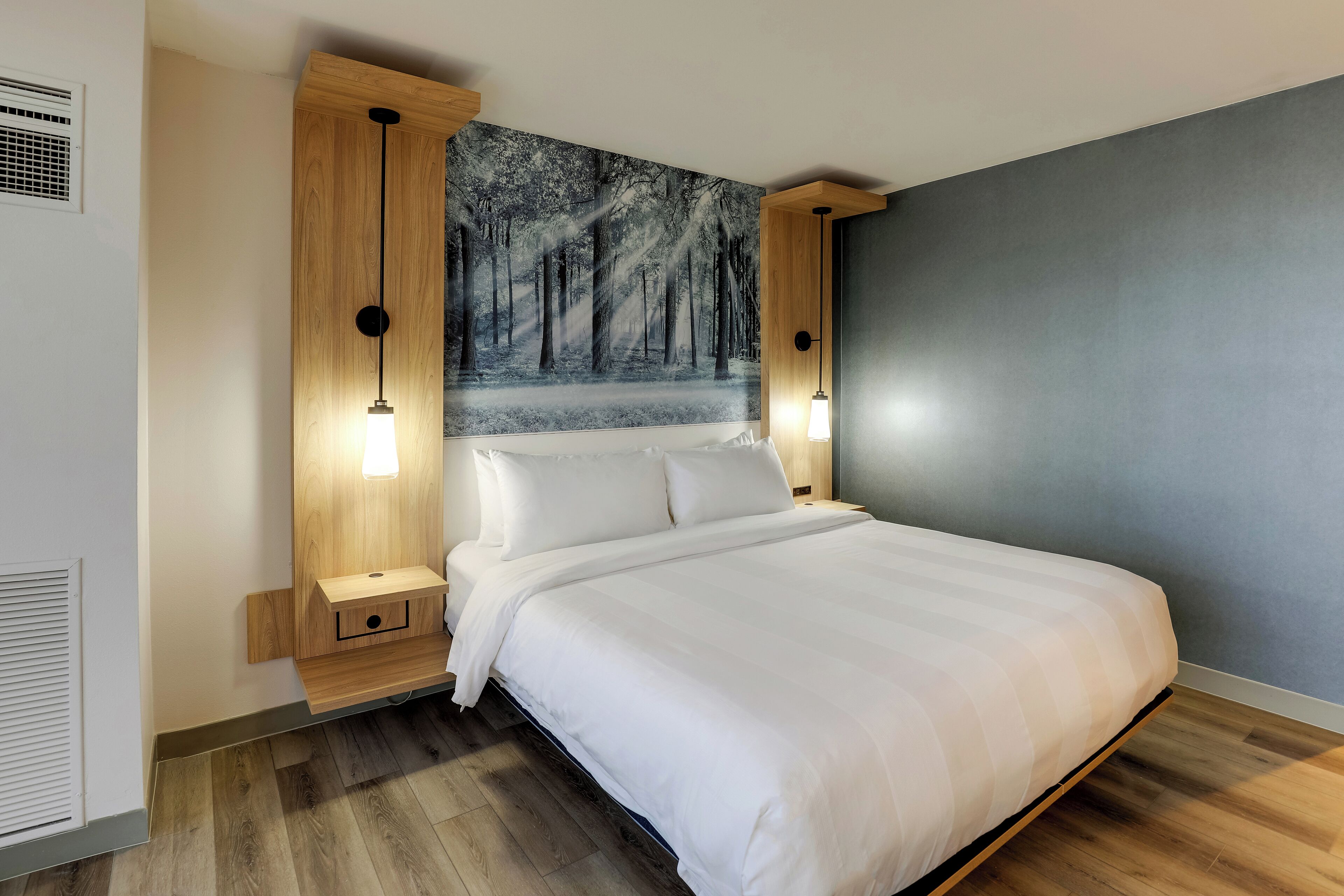 A modern bedroom with a large bed, wooden headboard, and a forest-themed wall mural.