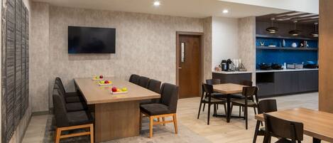 Un comedor moderno con una mesa de madera, sillas acolchadas y un televisor de pantalla plana en la pared.