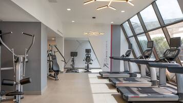 A modern gym with cardio equipment, including treadmills and ellipticals, and large windows providing natural light.