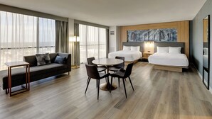 A hotel room with a bed, a sofa, a dining table with chairs, and a large window with curtains. - Mobile Marriott (Mobile)