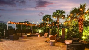 An outdoor patio area with seating arrangements, string lights, and palm trees. - Mobile Marriott (Mobile)