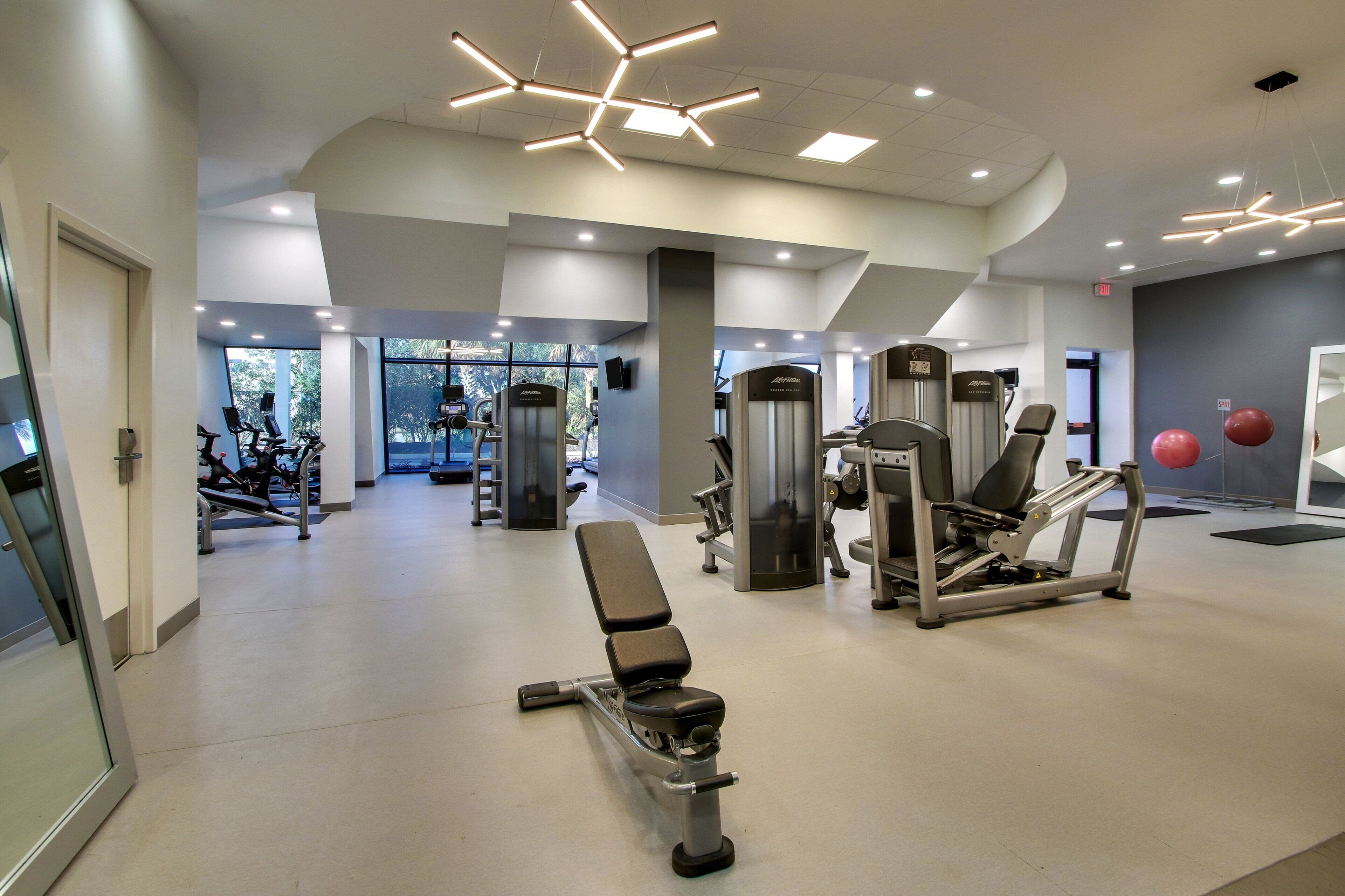 Ett modernt gym med olika typer av träningsutrustning, en bänk och ett stort fönster som släpper in naturligt ljus.