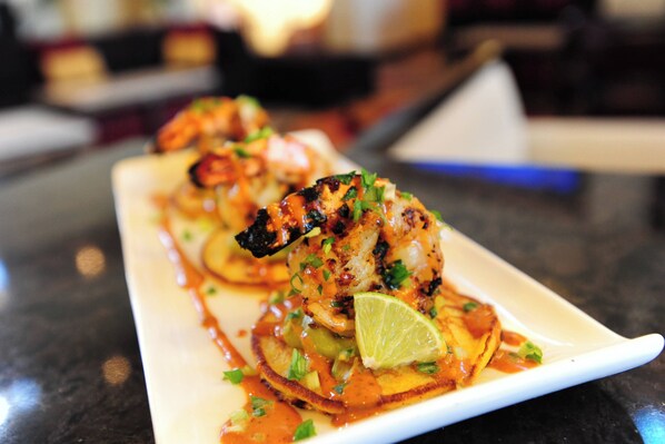 A dish of grilled shrimp on a white plate with a side of sauce and lime.
