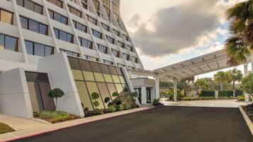 Un hotel moderno con fachada geométrica, vestíbulo cubierto y jardines ajardinados.