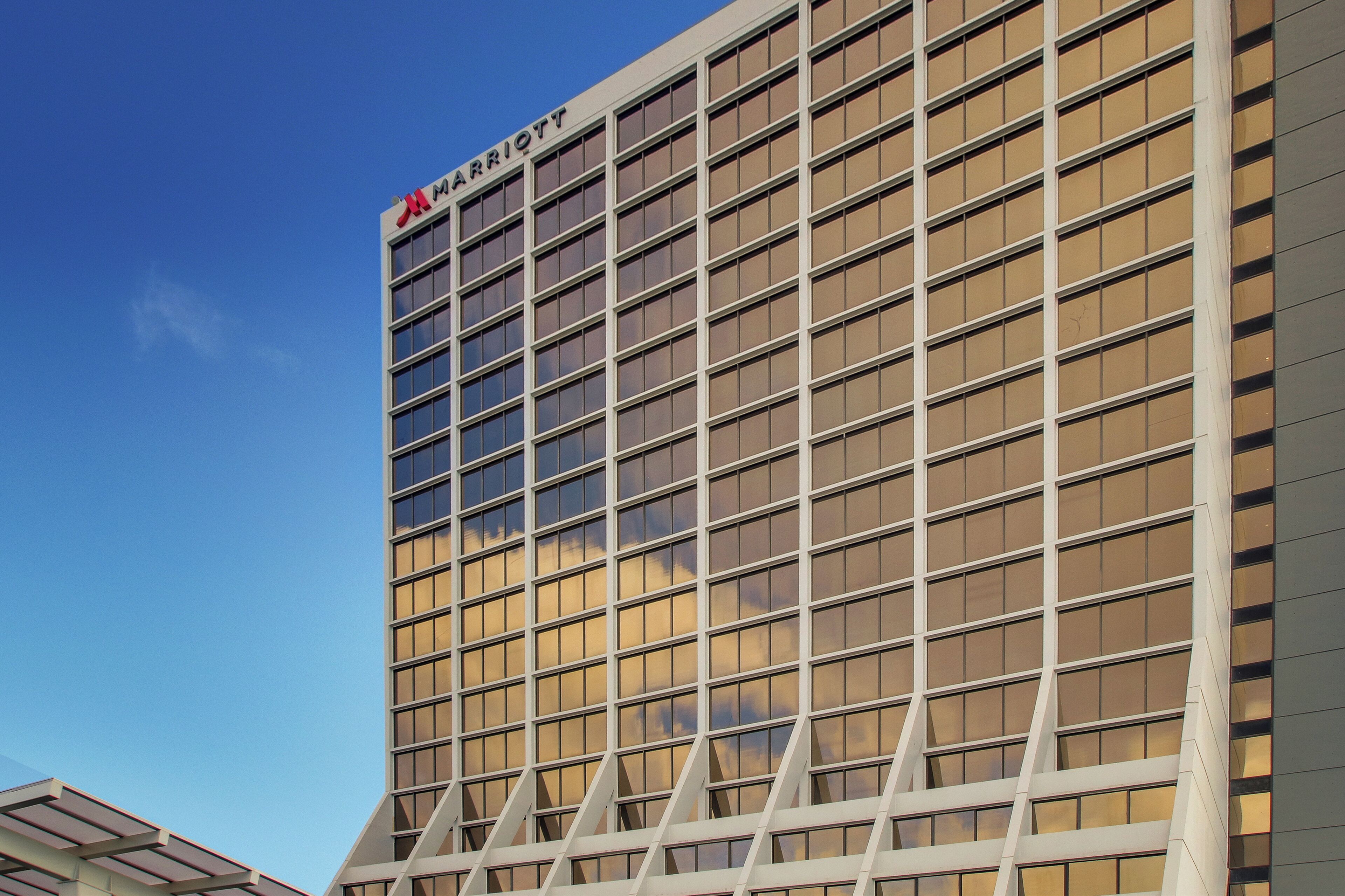 Un moderno edificio de hotel con una fachada de ventanas en forma de cuadrícula y un llamativo letrero con la palabra 'Marriott' en la parte superior.