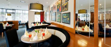 A modern hotel dining area with round tables, black cushioned seating, and artwork on the walls.
