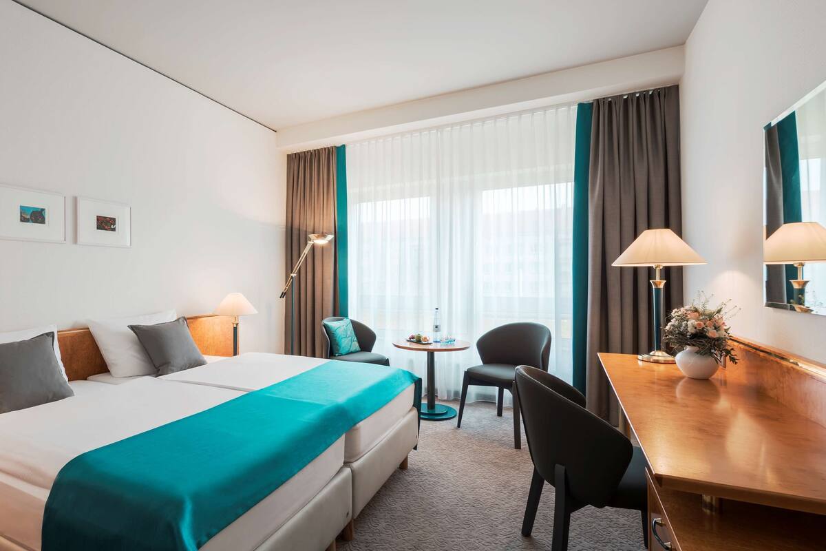 Hotelkamer met een bed, twee stoelen, een tafeltje, een lamp en een bloemenvaas.