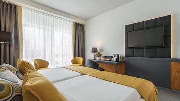 A hotel room with two beds, a desk with a lamp, a coffee maker, and a TV mounted on the wall.