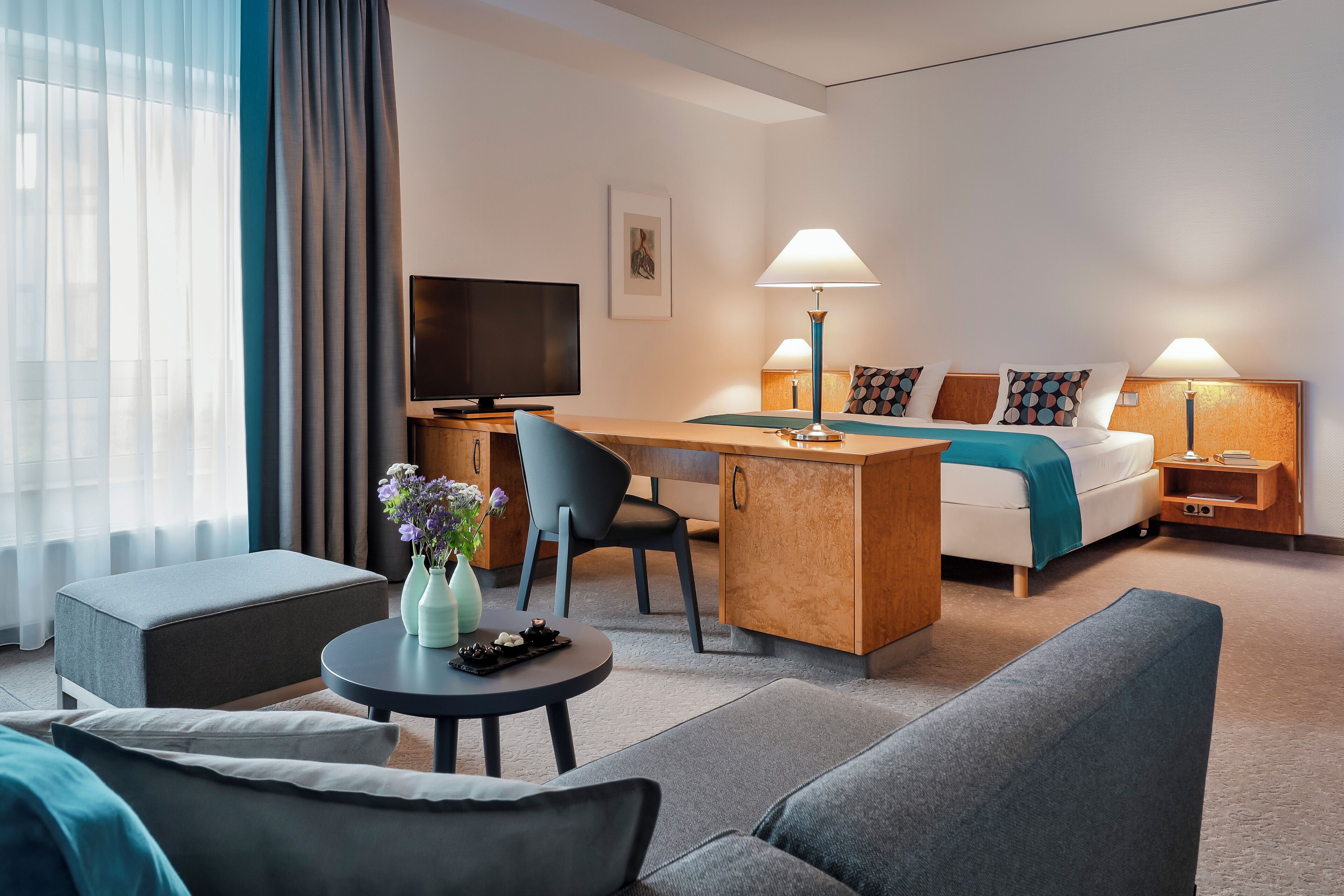 Ett modernt hotellrum med en säng, ett skrivbord, en TV, en soffa och ett soffbord.