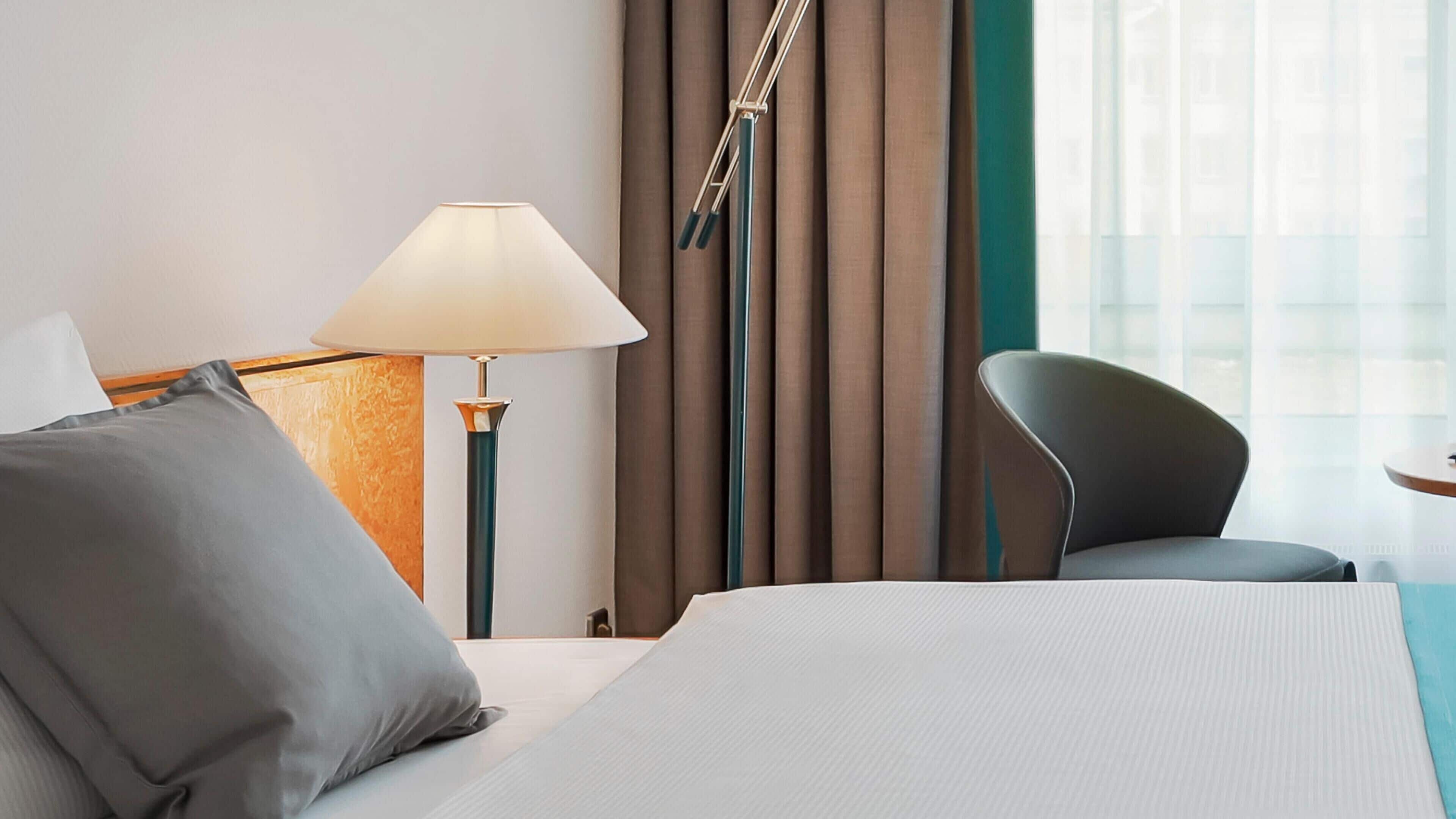 Habitación de hotel con cama, escritorio, silla, lámpara y cortinas.
