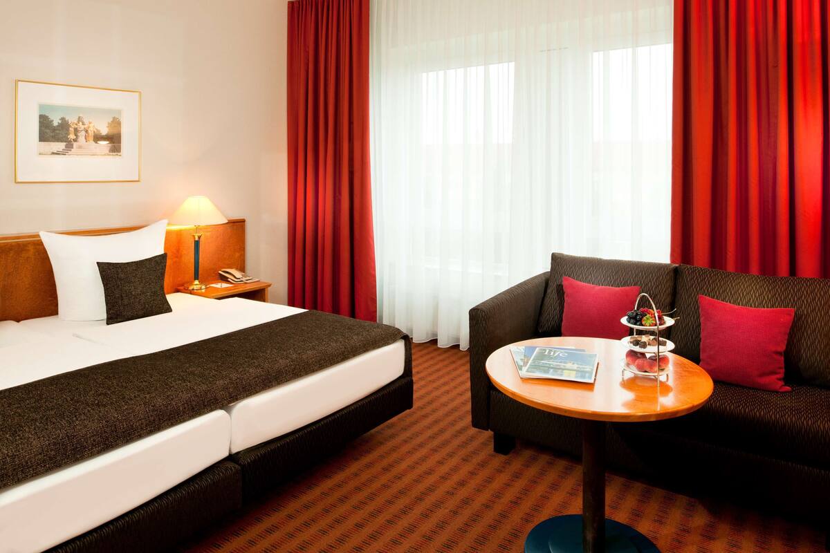 Een hotelkamer met een bed, een bank, een kleine tafel met een fruitschaal, een lamp en een lijst aan de muur.