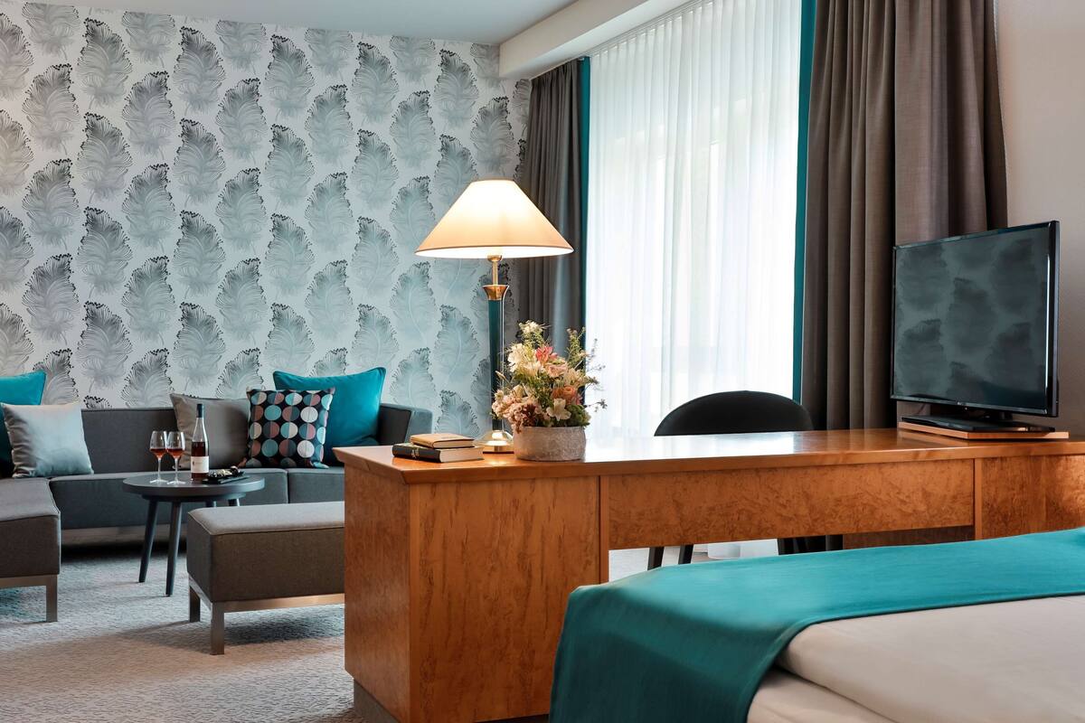 Een hotelkamer met een bank, een bureau met lamp, een televisie en een raam met gordijnen.