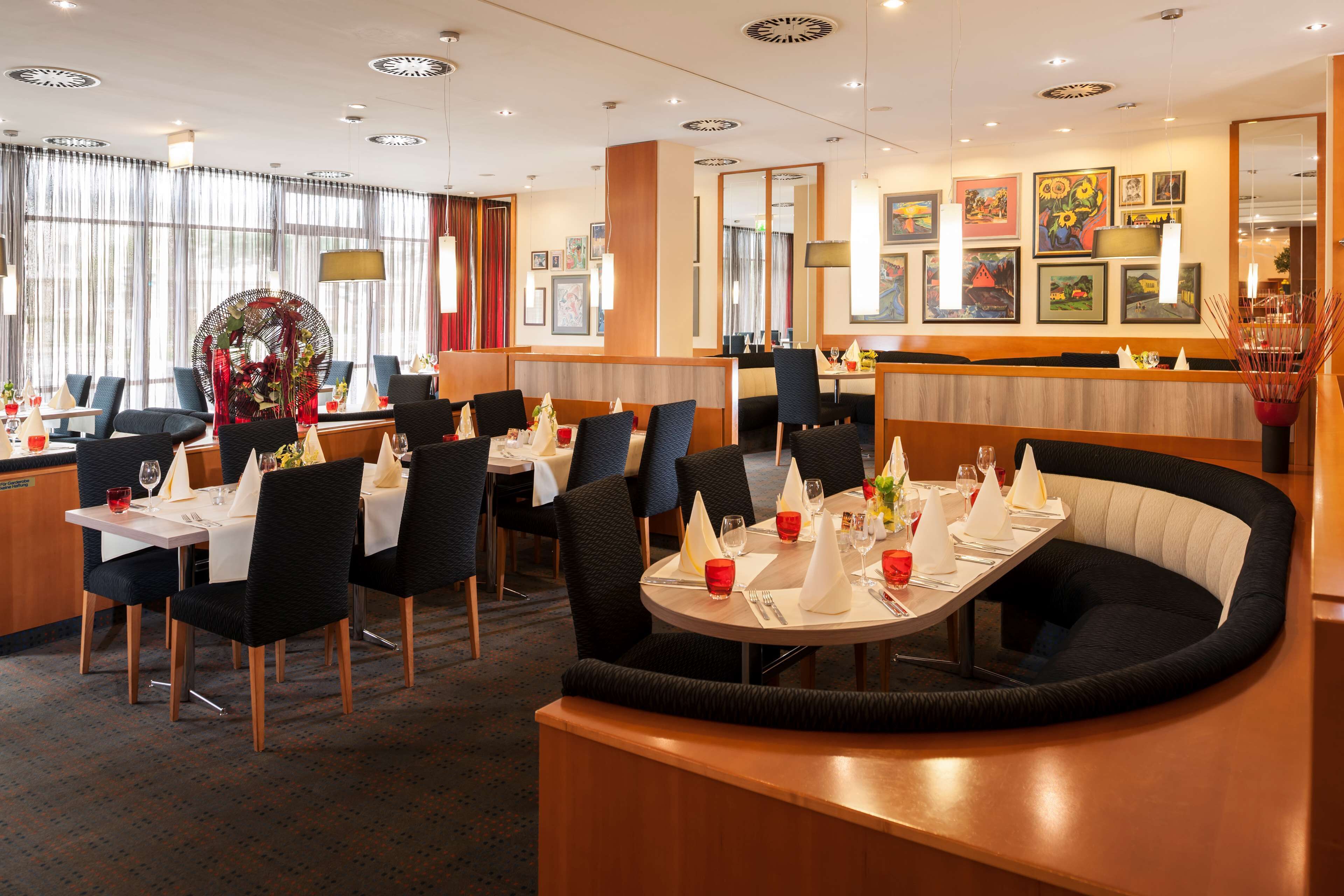 A hotel dining area with round tables, black upholstered booths, and a bar counter.