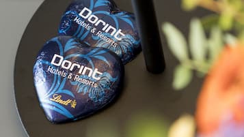 Zwei herzförmige Pralinen mit dem Branding 'DORINT Hotels & Resorts', platziert auf einer dunklen Oberfläche mit einem Stift und etwas Grün im Vordergrund.