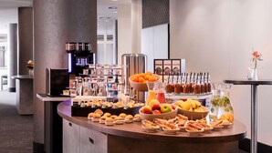 Un bufé con diversos alimentos y bebidas, como frutas, sándwiches y una máquina de café.