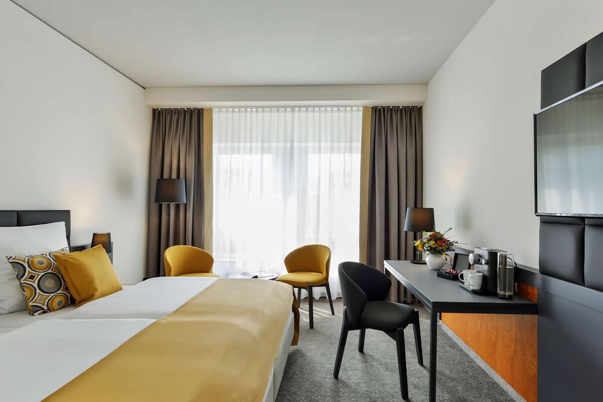 Een hotelkamer met een bed, twee stoelen, een bureau, een televisie en een raam met gordijnen.